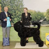 A man and woman standing next to a black dog.
