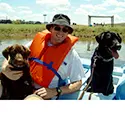 A man and two dogs on a boat in the water.