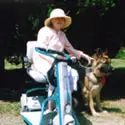 A woman riding on the back of a scooter with a dog.